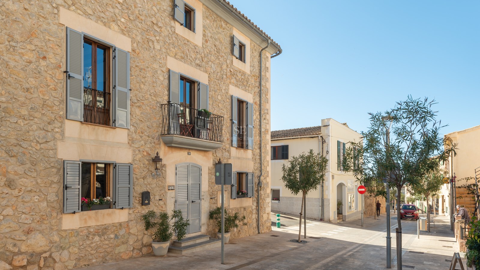 Immeuble en pierre traditionnelle avec volets gris et balcons en fer dans une rue ensoleillée.
