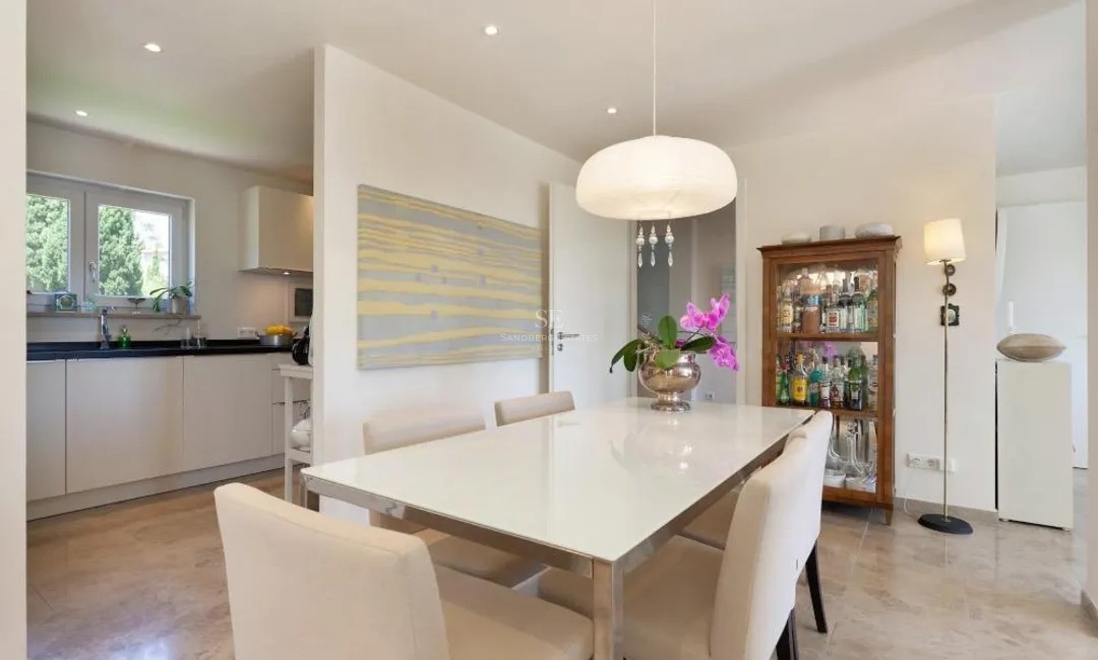 Contemporary dining room with marble floors, a white dining table, and cream chairs next to a modern kitchen.