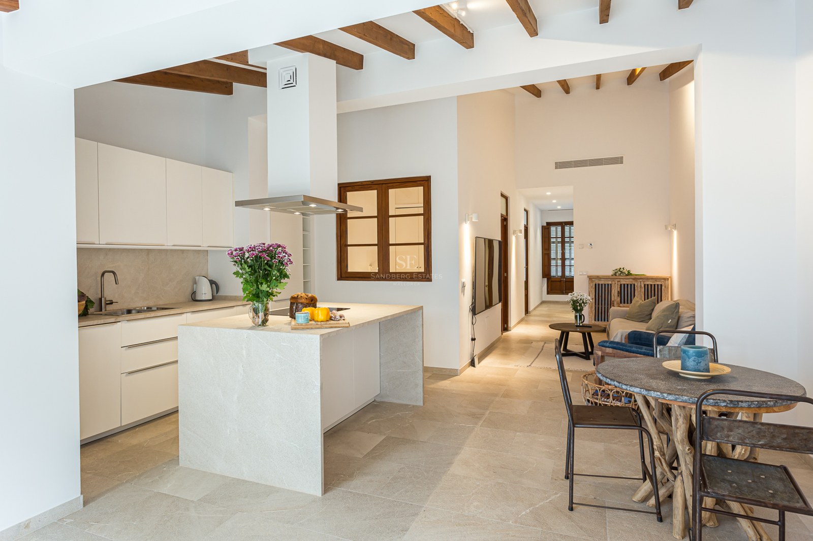 Cocina luminosa con isla de piedra, vigas de madera en el techo y zona de comedor rústica.