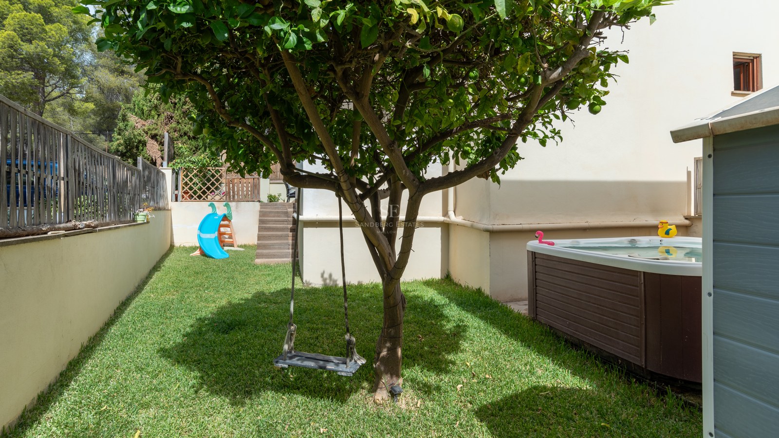 Jardín con césped, columpio en un árbol, tobogán azul y jacuzzi exterior revestido de madera.