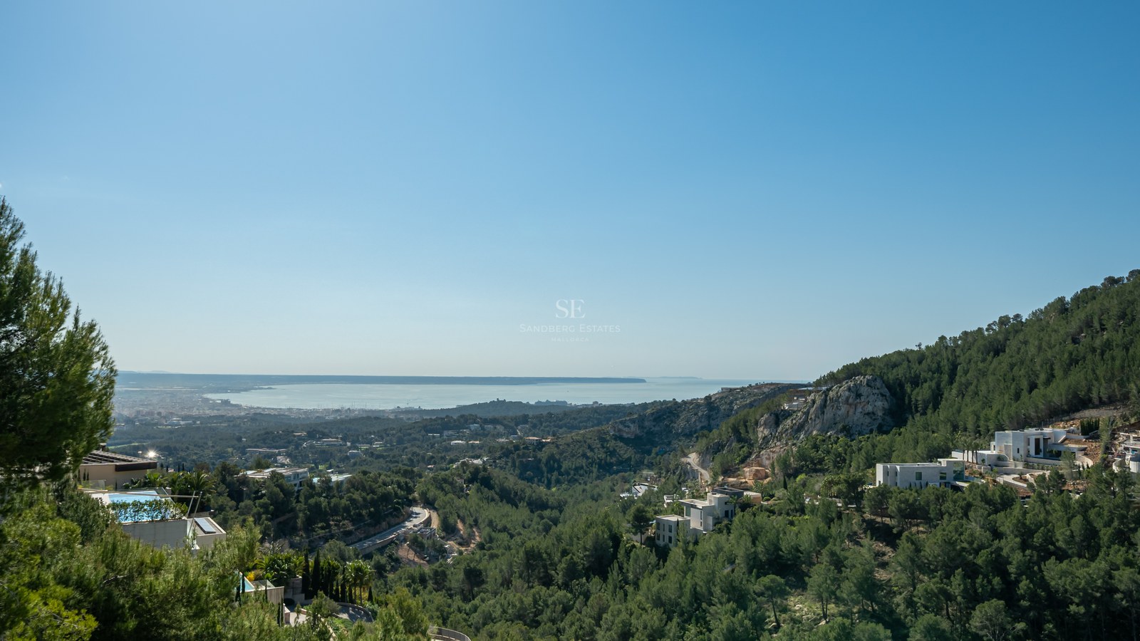 Villas blancas modernas entre pinos con vistas al mar Mediterráneo bajo un cielo azul despejado.