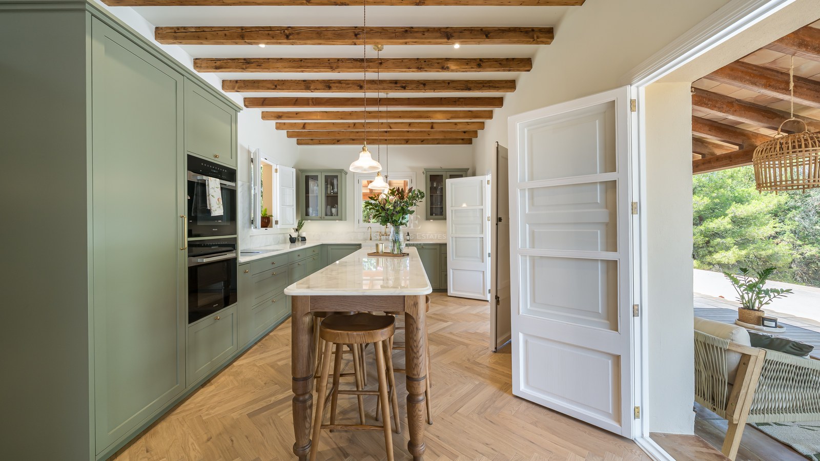 Luxury kitchen featuring sage green cabinets, marble-topped island, herringbone wood floors, and rustic ceiling beams.
