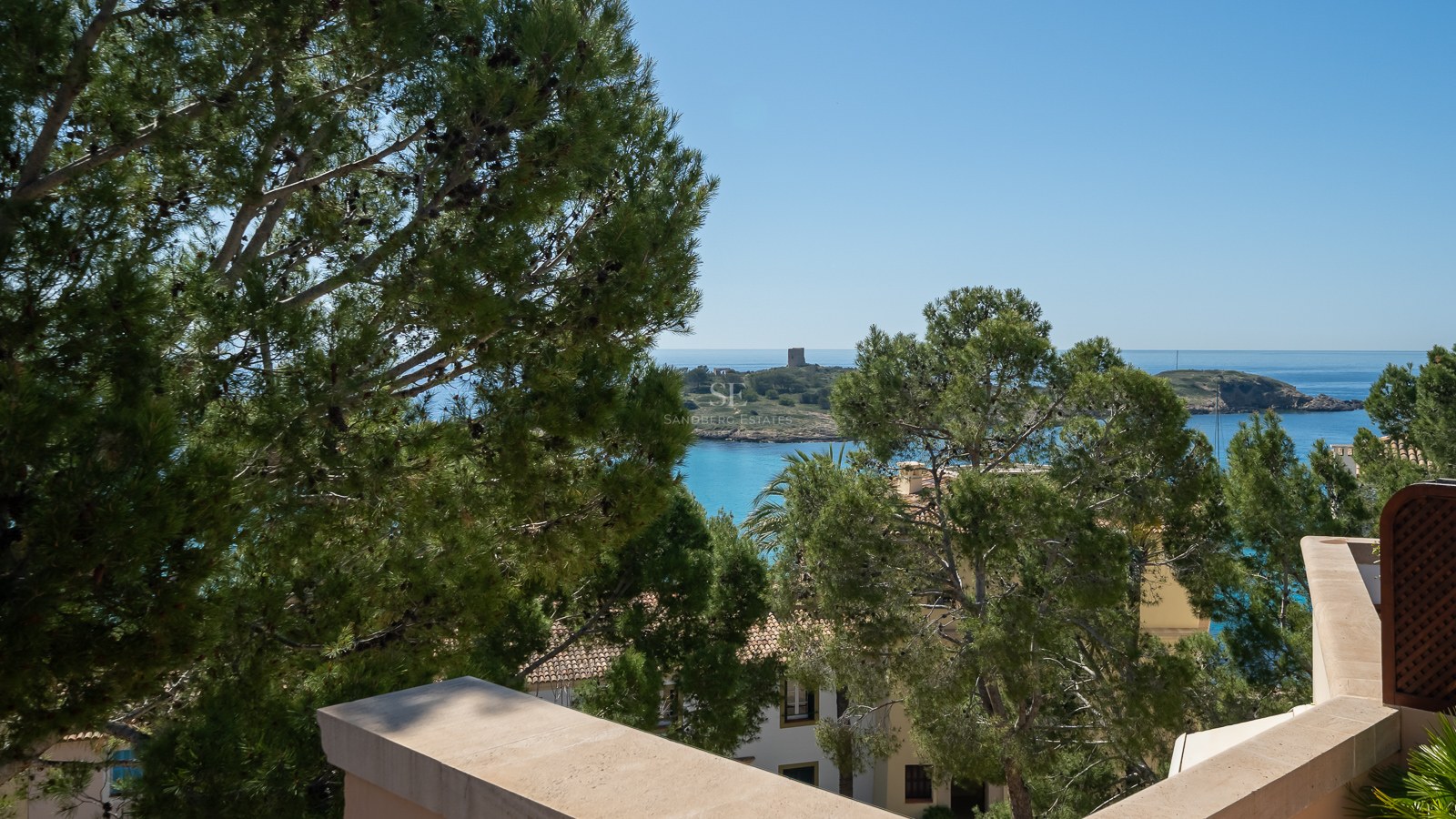 Vue depuis une terrasse en pierre sur la mer Méditerranée turquoise avec des pins et une petite île au loin.