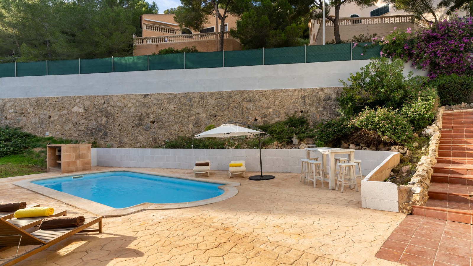 Private swimming pool with lounge chairs, white umbrella, and a rustic stone wall background.