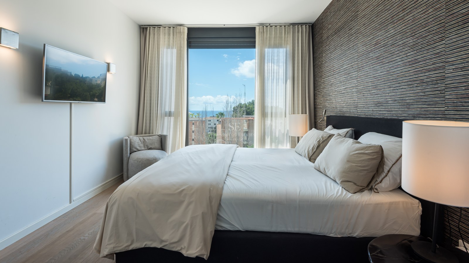 Contemporary bedroom featuring a double bed, textured accent wall, and a large window overlooking the sea.
