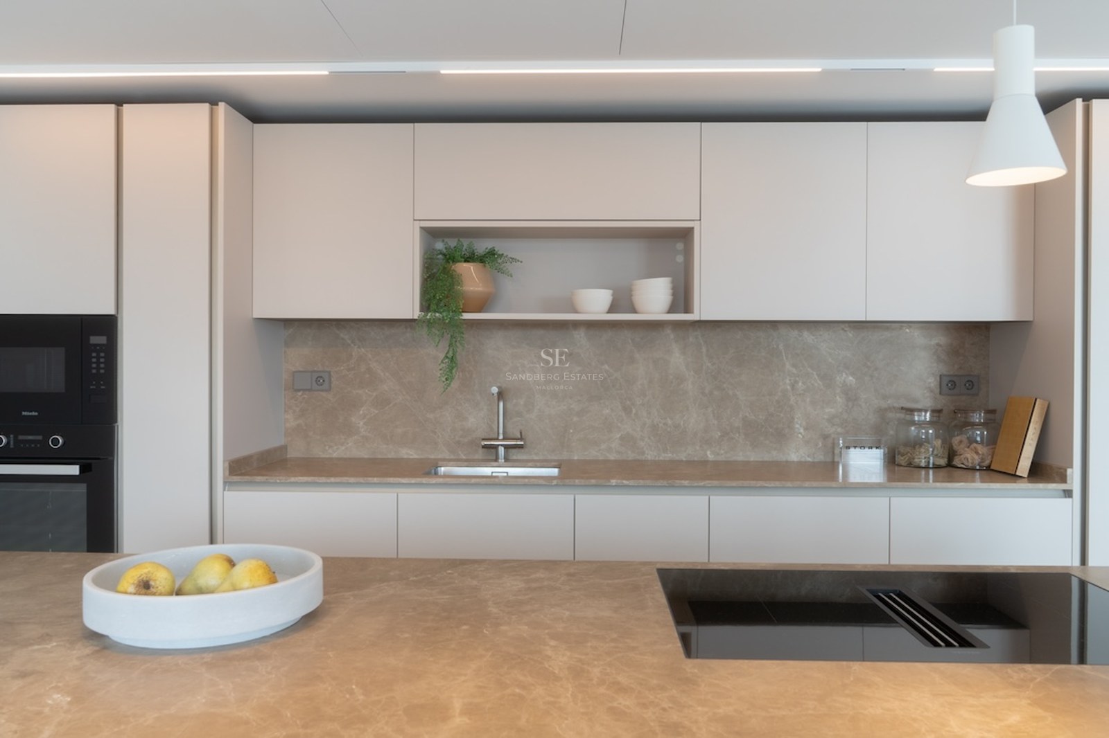 Modernt kök med bänkskivor i beige sten, mattvita skåp och inbyggda Miele-vitvaror.
