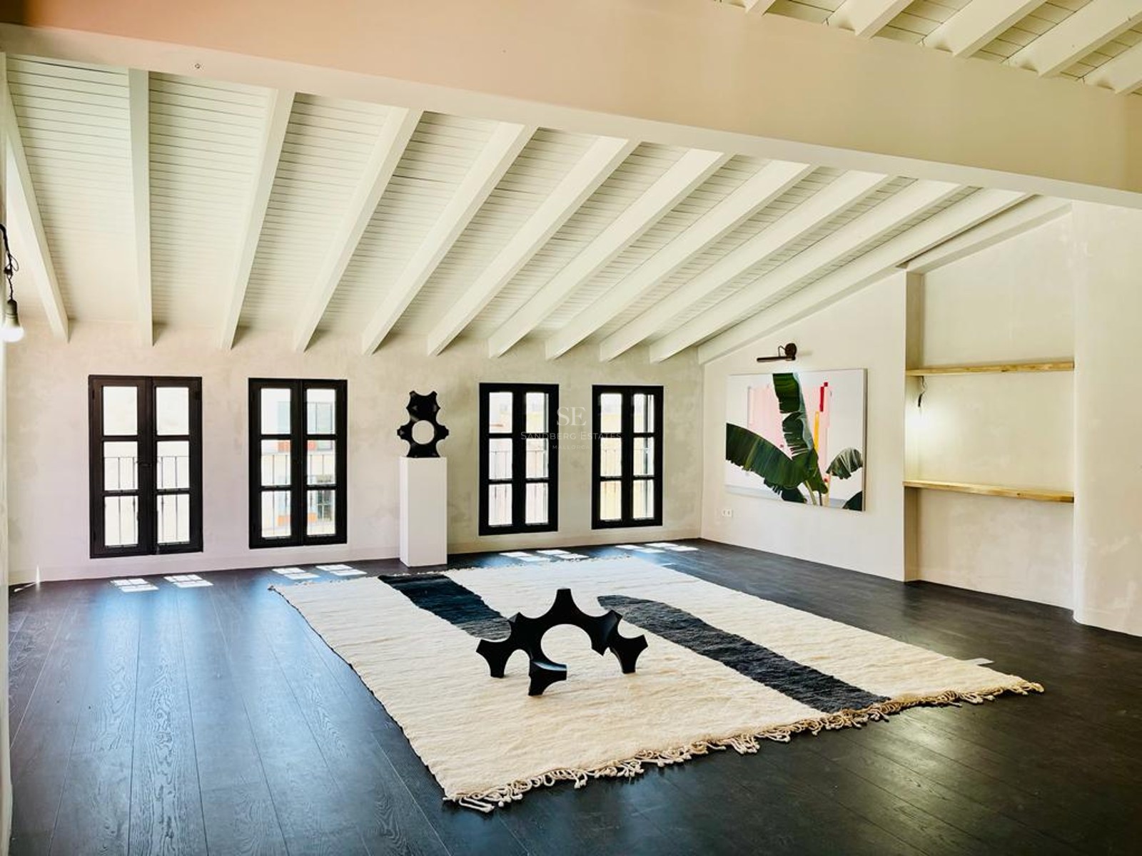 Pièce minimaliste avec parquet en bois foncé, plafond à poutres blanches et fenêtres à cadres noirs.