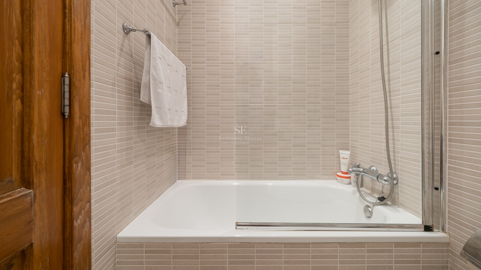 Baignoire blanche encastrée avec paroi vitrée et carrelage beige dans une salle de bain lumineuse.