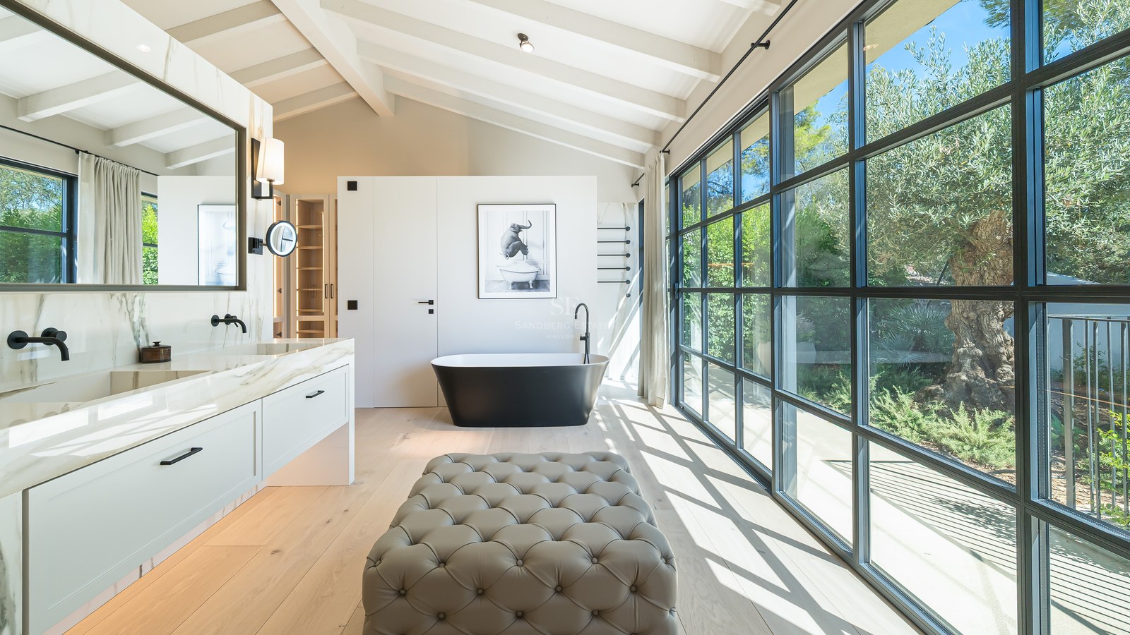 Luxury bathroom with a freestanding black tub, marble double vanity, and floor-to-ceiling windows facing a garden.