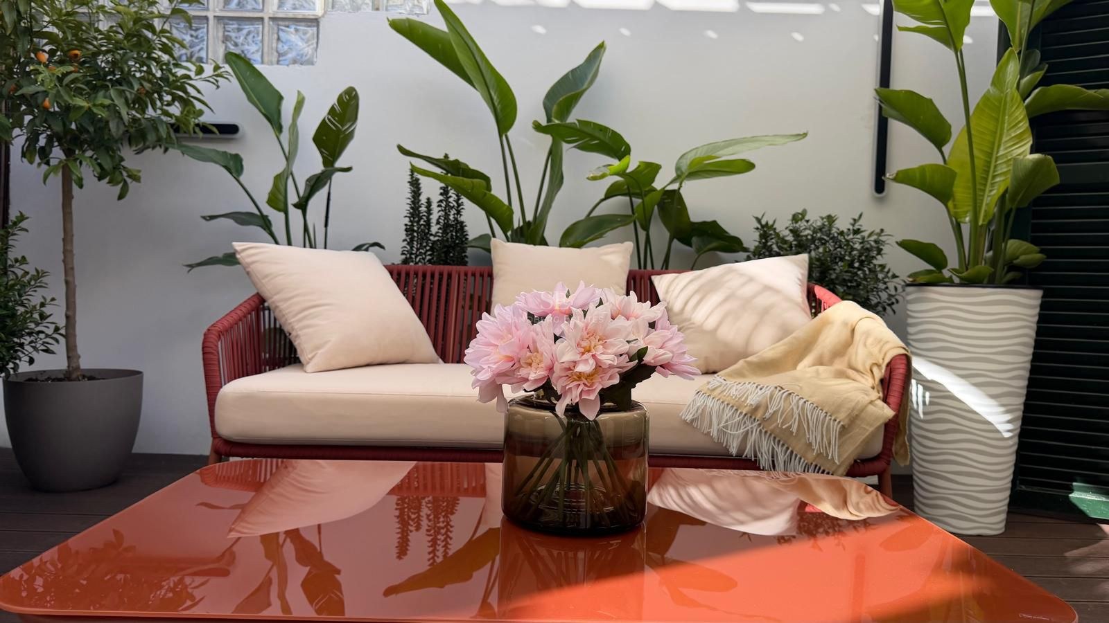 Canapé en corde rouge avec coussins crème sur une terrasse entourée de plantes tropicales et une table basse brillante.