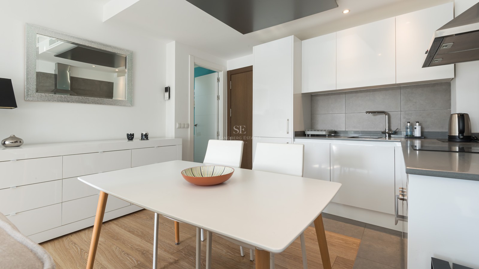 Bright modern kitchen with white cabinetry, a grey backsplash, and a white dining table with wooden legs.