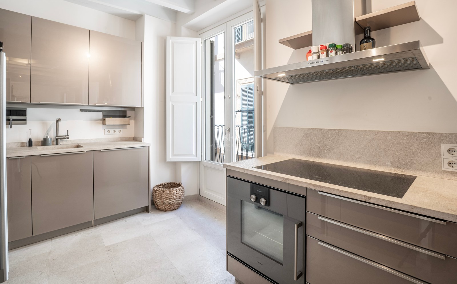 Bright modern kitchen with taupe glossy cabinets, stone countertops, integrated oven, and a balcony door.