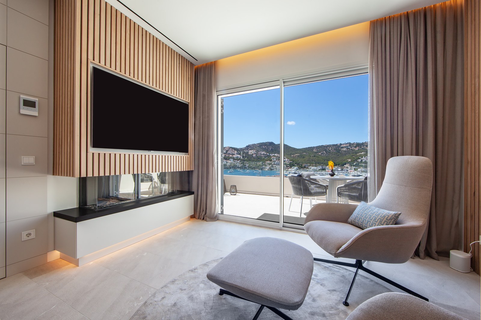 Contemporary lounge featuring an armchair, fireplace, wood-slat TV wall, and panoramic harbor views through sliding doors.