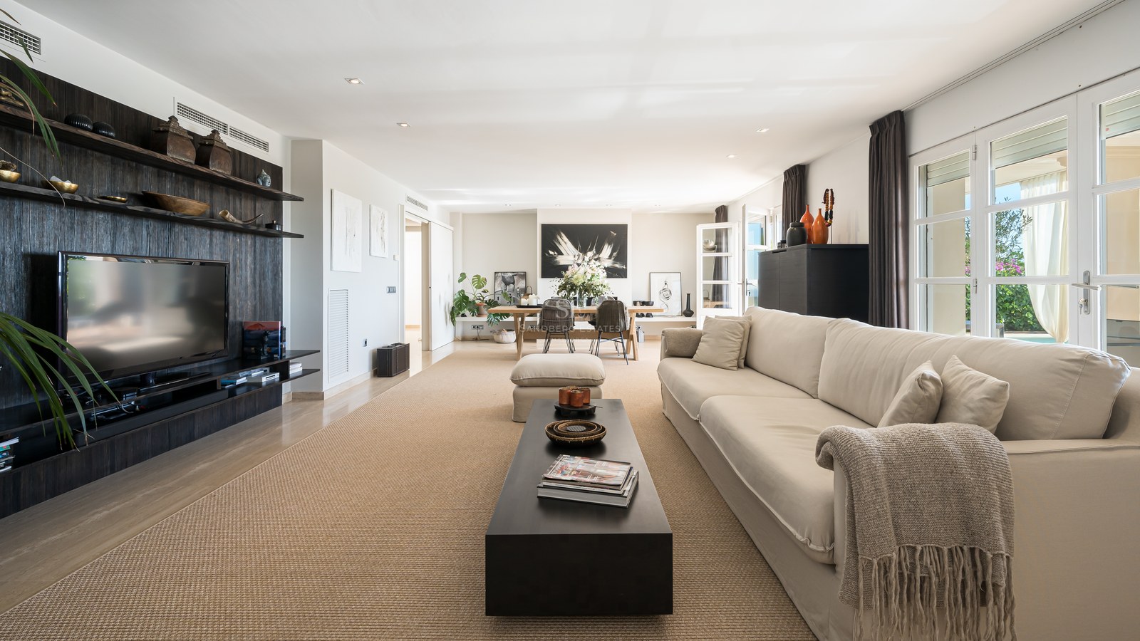 Vaste salon avec canapé beige, meuble multimédia en bois sombre, tapis en fibres naturelles et baies vitrées.