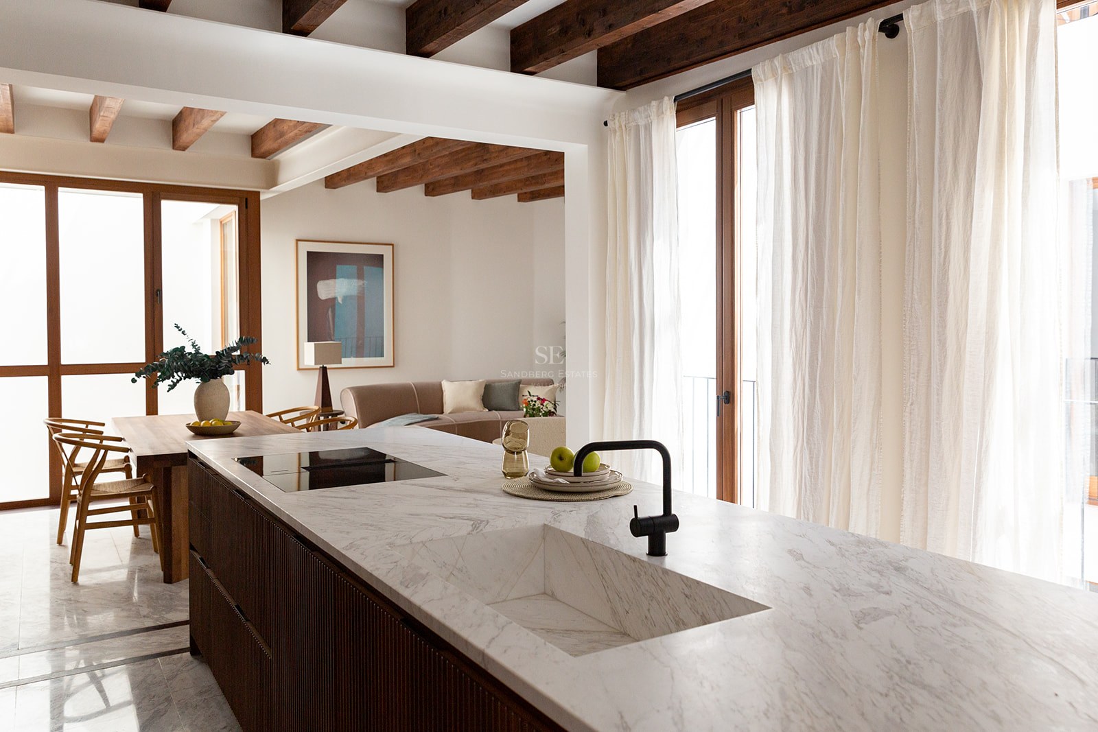 Modern kitchen featuring a white marble island with integrated sink, dark wood cabinetry, and exposed ceiling beams.
