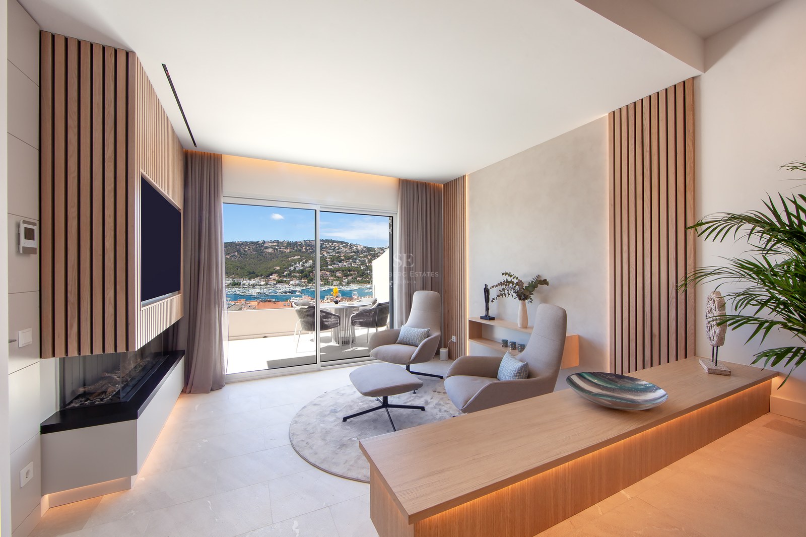 Modern lounge with wood slats, designer chairs, and a sliding glass door revealing a stunning Mediterranean harbor view.