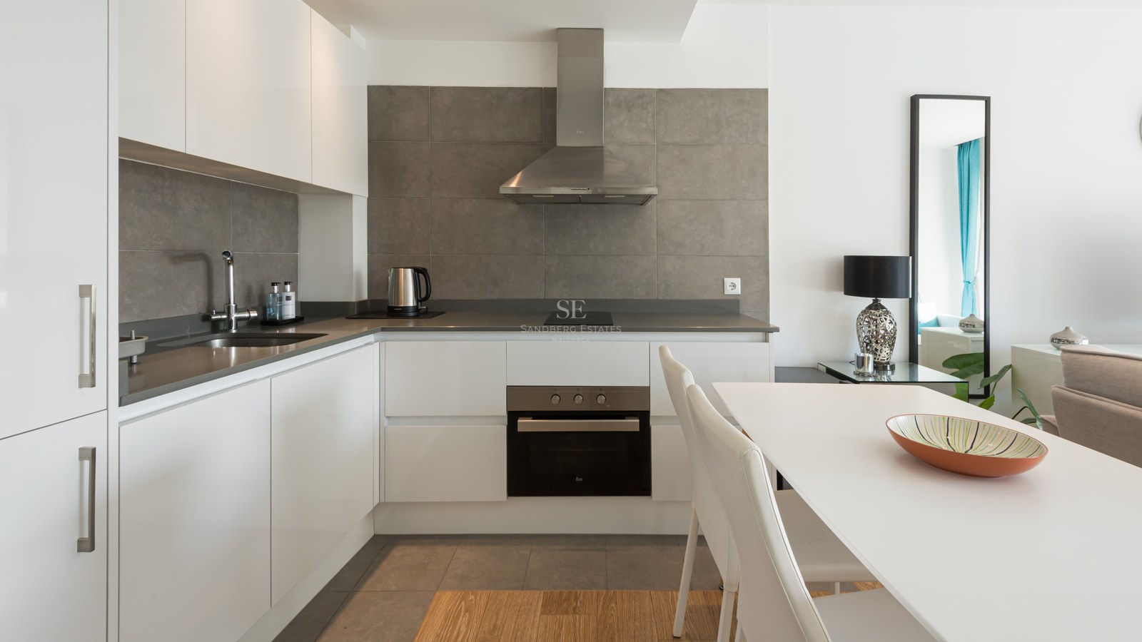 Modern white kitchen with grey tile backsplash, stainless steel appliances, and white dining table.
