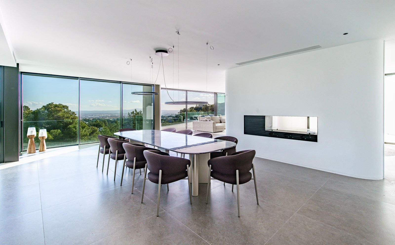 Salle à manger moderne élégante avec une grande table, des chaises sombres et des baies vitrées donnant sur la nature.