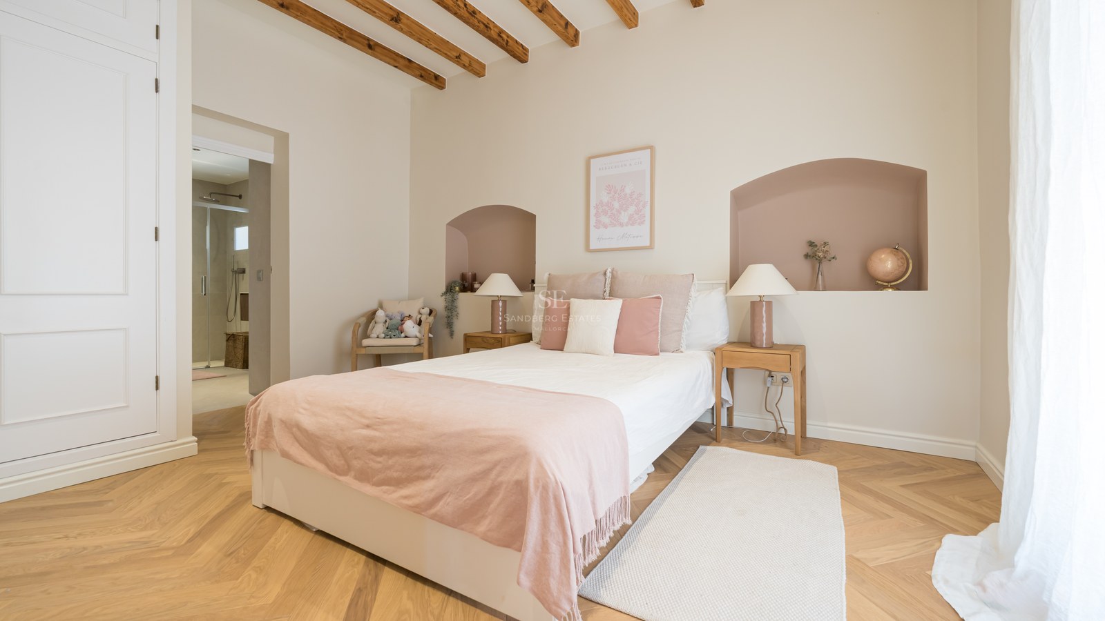 Bright bedroom with herringbone oak floors, wooden ceiling beams, a double bed, and an adjoining ensuite bathroom.