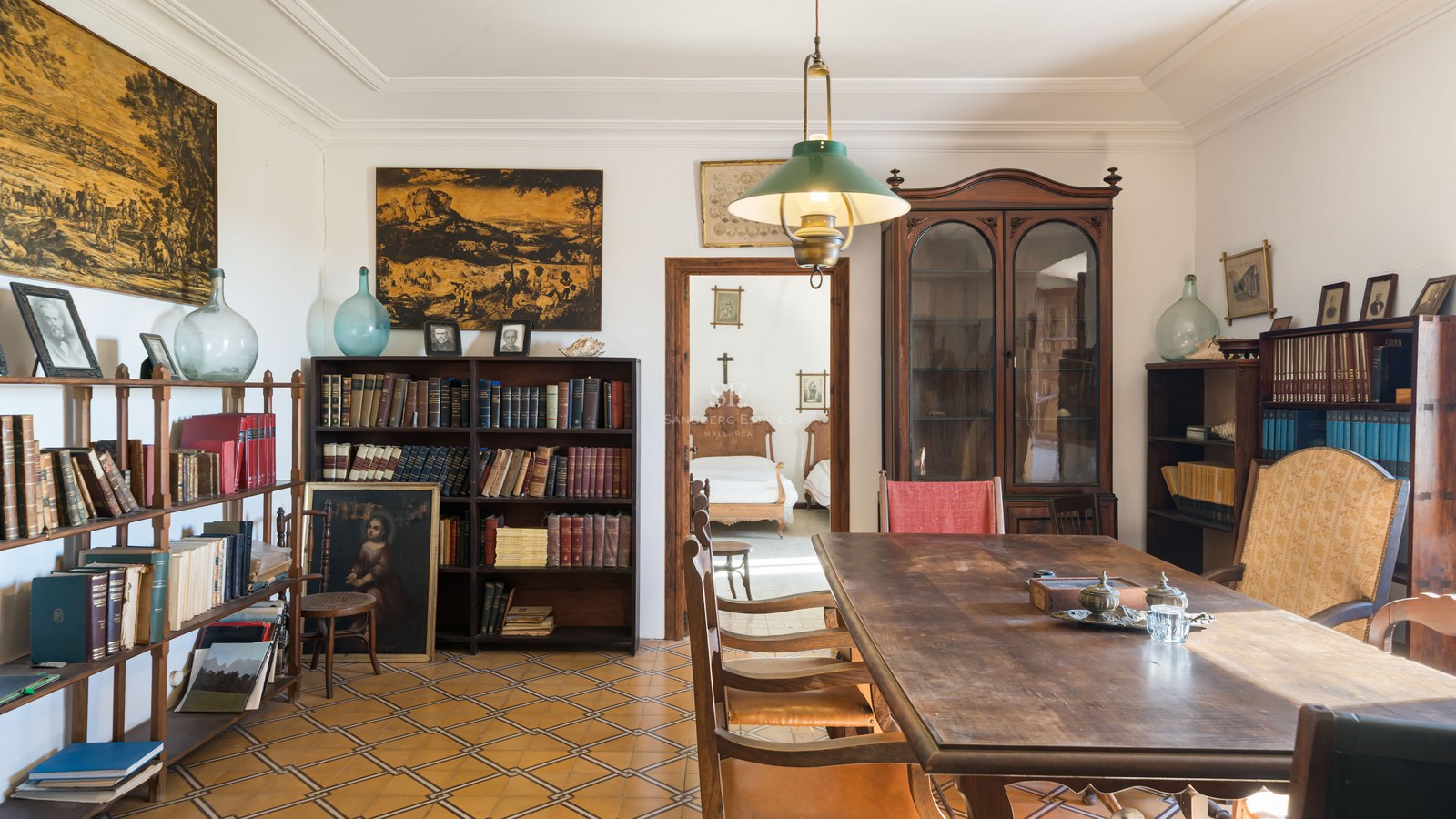 Habitación clásica con gran mesa de madera, estanterías repletas de libros y suelo de baldosas decoradas.