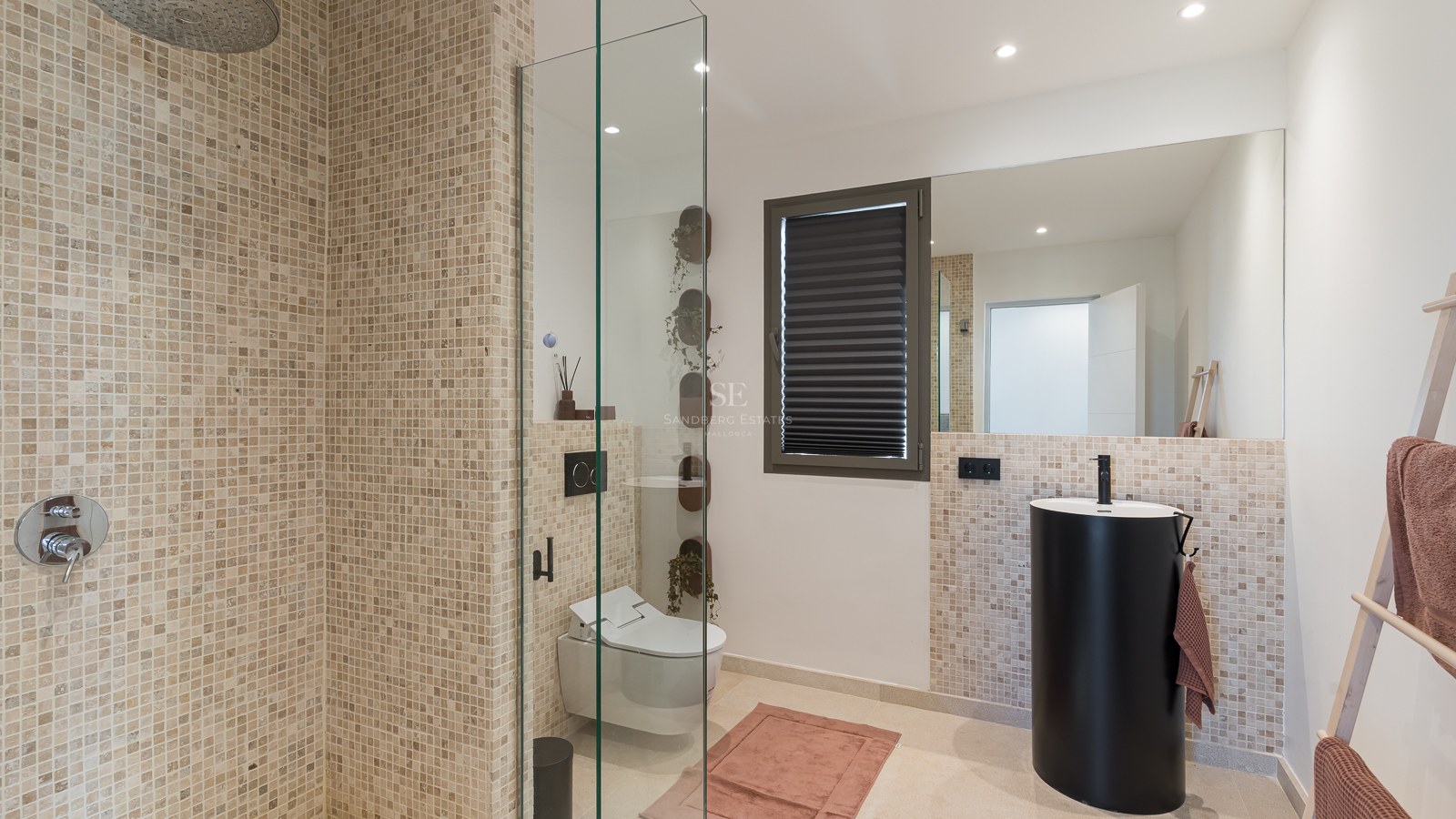 Modernes Badezimmer mit Mosaikfliesen, Glasduschwand, mattschwarzem Säulenwaschbecken und Wand-WC.