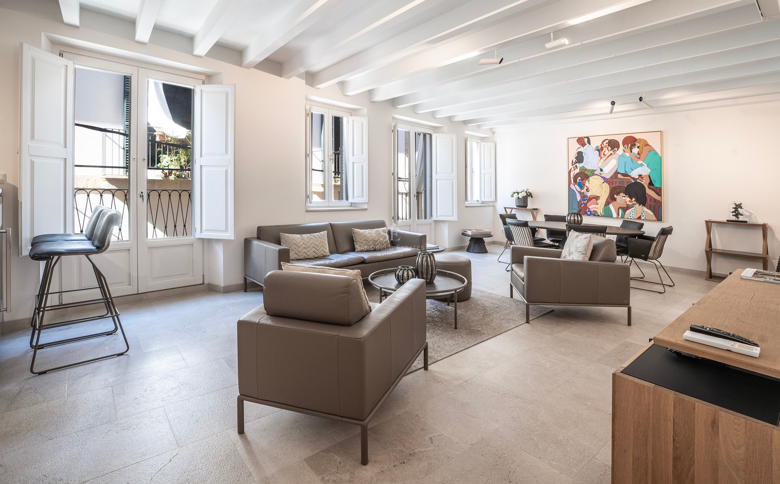 Bright living room with grey leather sofas, white beamed ceiling, and a dining area featuring a colorful art piece.