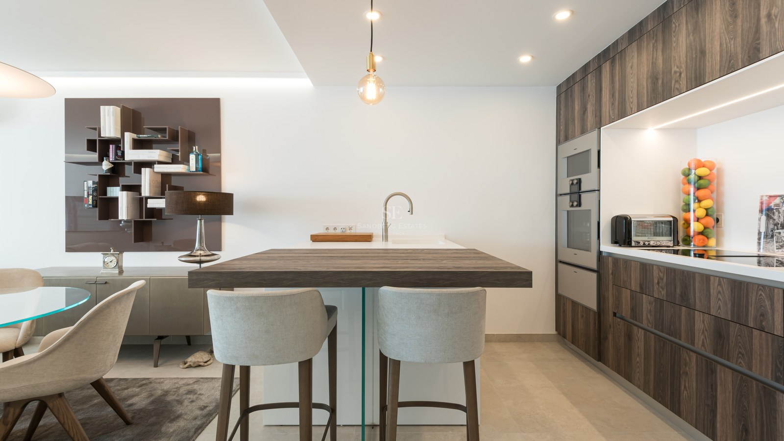 Modern kitchen featuring a dark wood island with grey bar stools, sleek cabinetry, and integrated high-end appliances.