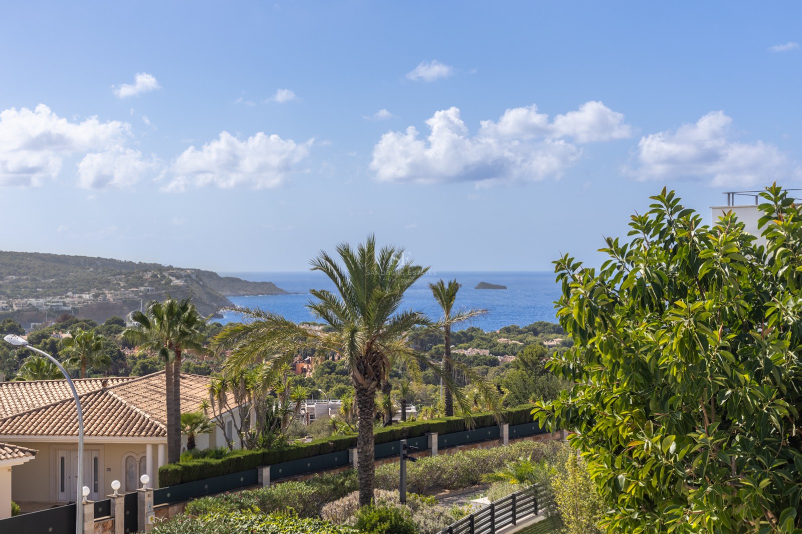 Vue surélevée d'un paysage côtier avec des palmiers, des toits en terre cuite et la mer Méditerranée bleue au loin.