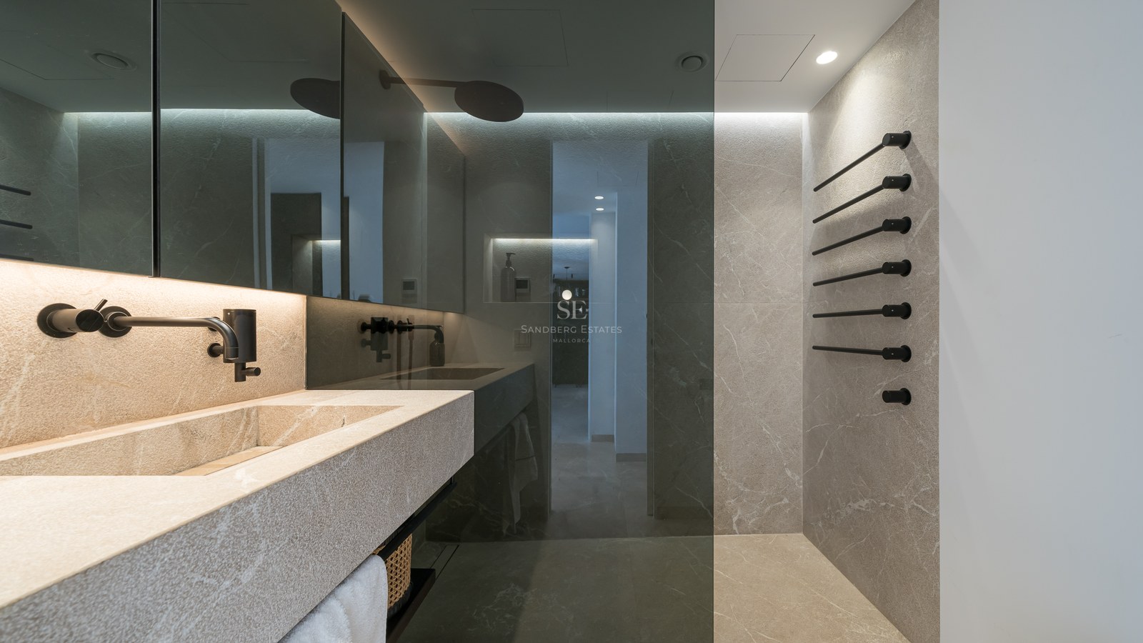 Salle de bain moderne avec lavabo en pierre, robinetterie noir mat et murs en pierre avec paroi de douche en verre.