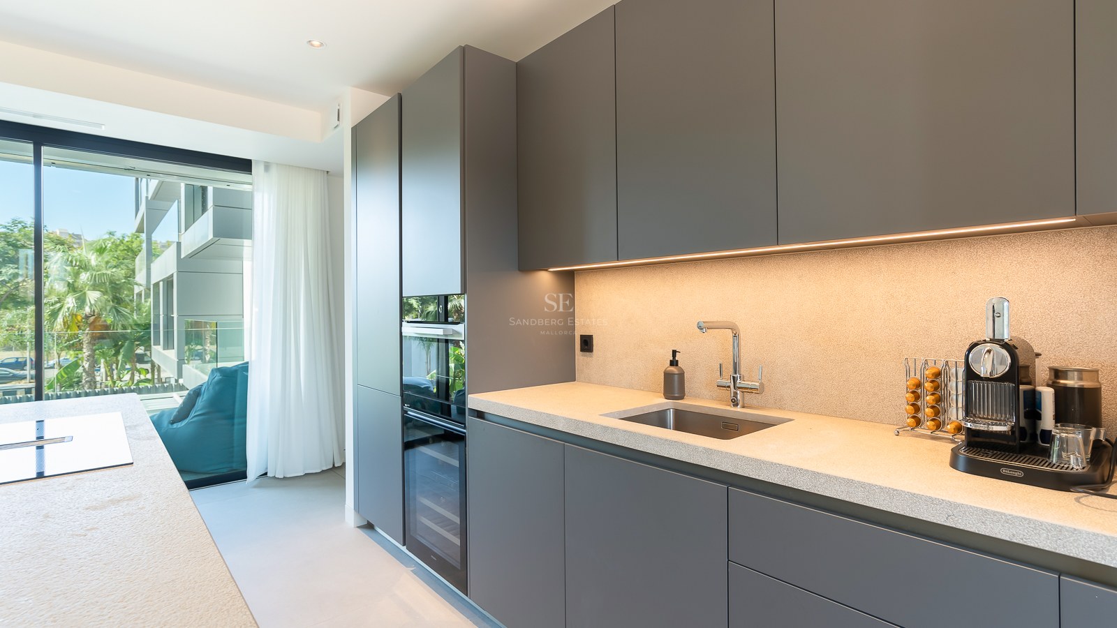 Cuisine contemporaine gris mat avec plan de travail en pierre, appareils intégrés et accès direct à la terrasse.