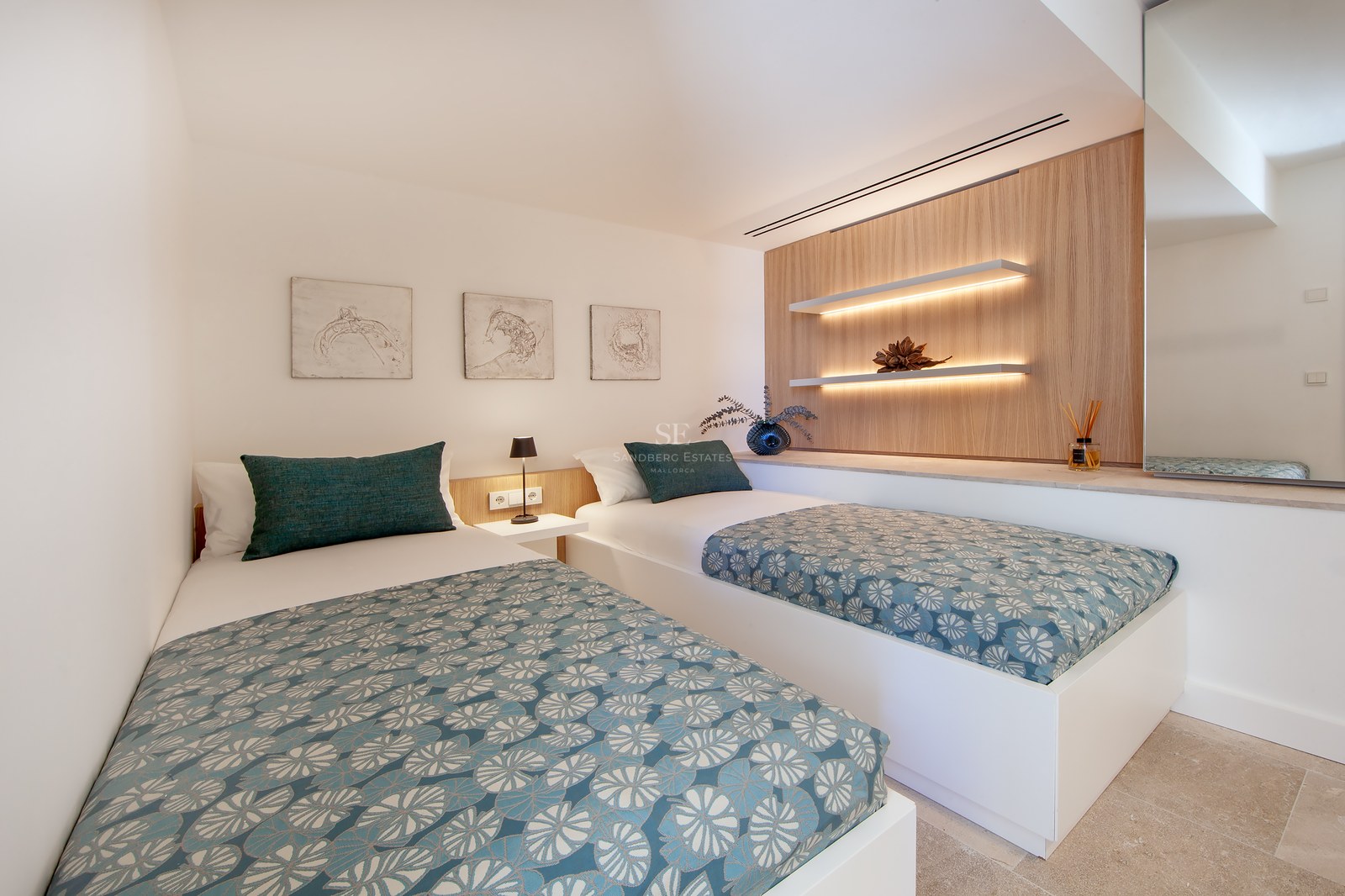 Modern bedroom featuring two single beds with teal patterned covers, wooden wall panels, and warm LED floating shelves.