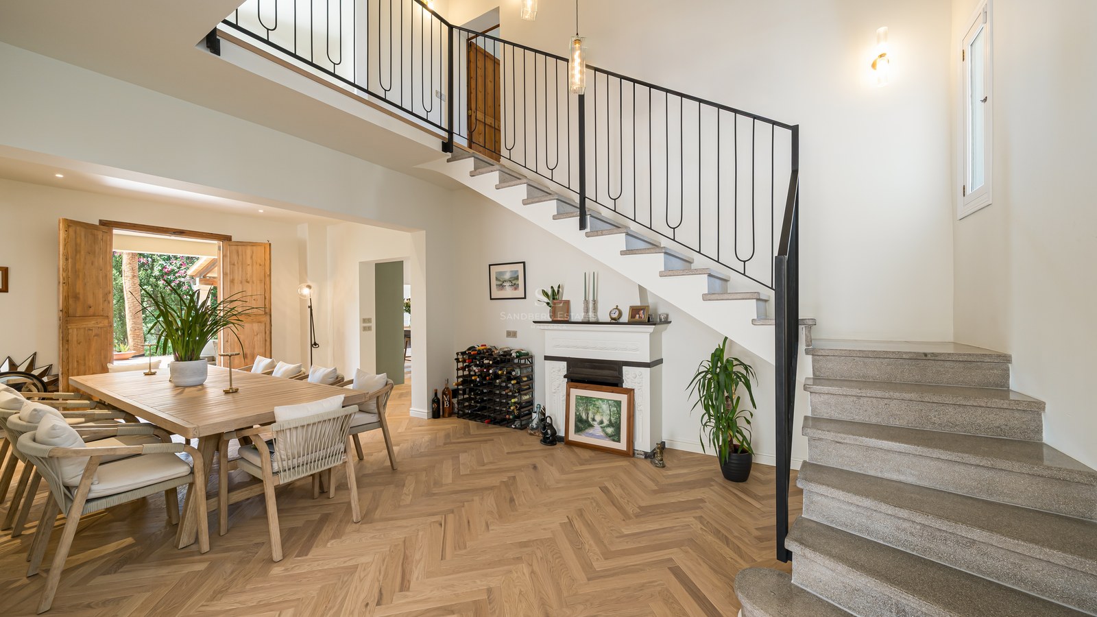 Dining area featuring an oak table, herringbone wood flooring, and a stone staircase with iron railings.