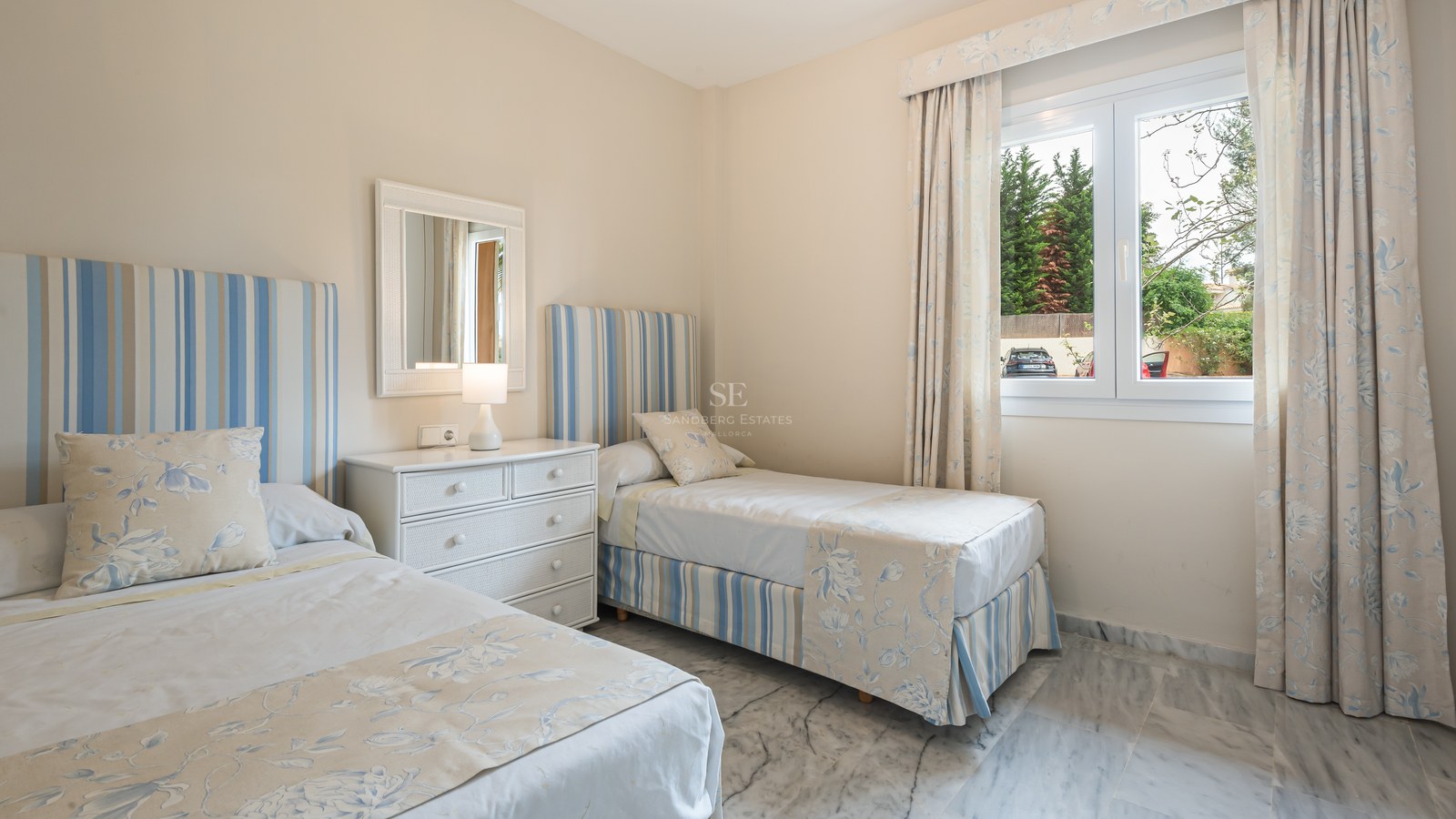 Chambre avec deux lits jumeaux, linge bleu et blanc, commode blanche et sol en marbre poli.