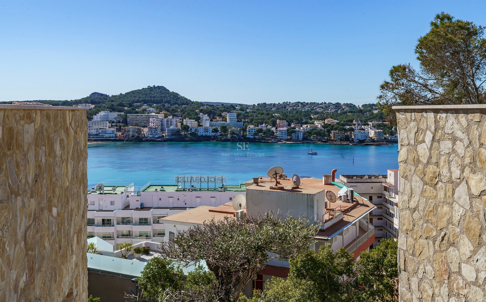 Vue d'une baie méditerranéenne turquoise encadrée par des murs en pierre naturelle sous un ciel bleu clair.