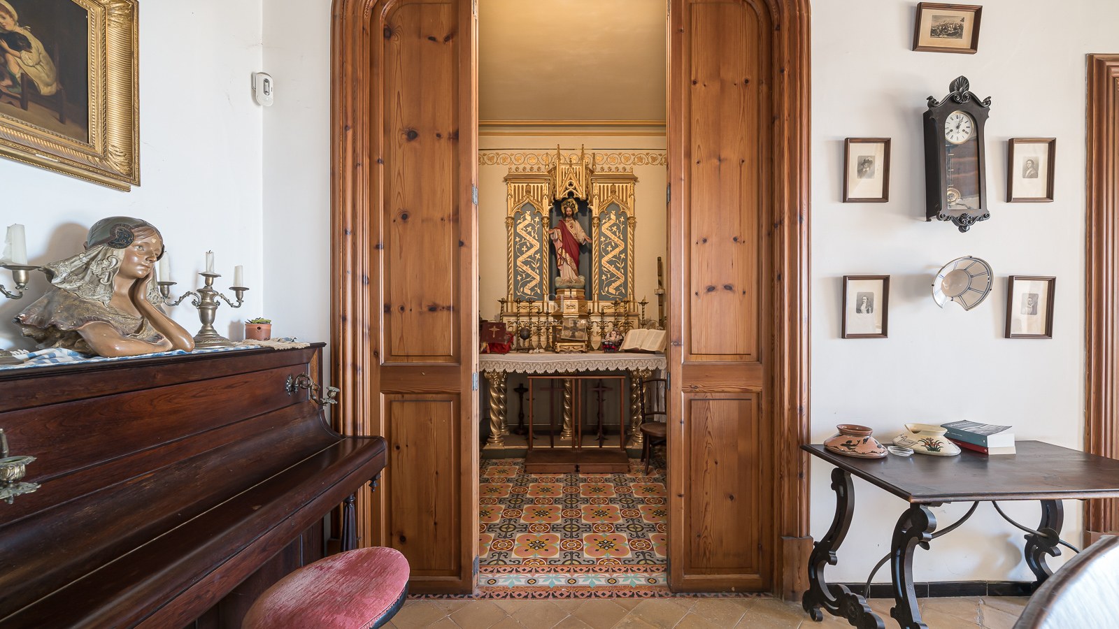 Vista a través de puertas de madera hacia una pequeña capilla privada ornamentada junto a un piano vertical.