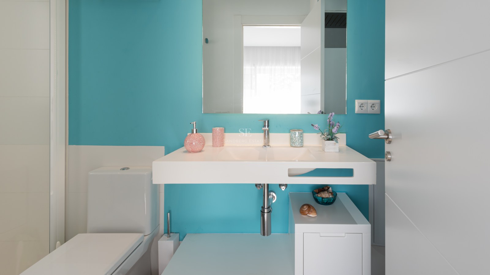 Modern bathroom with a vibrant turquoise wall, floating white sink, large mirror, and white toilet.