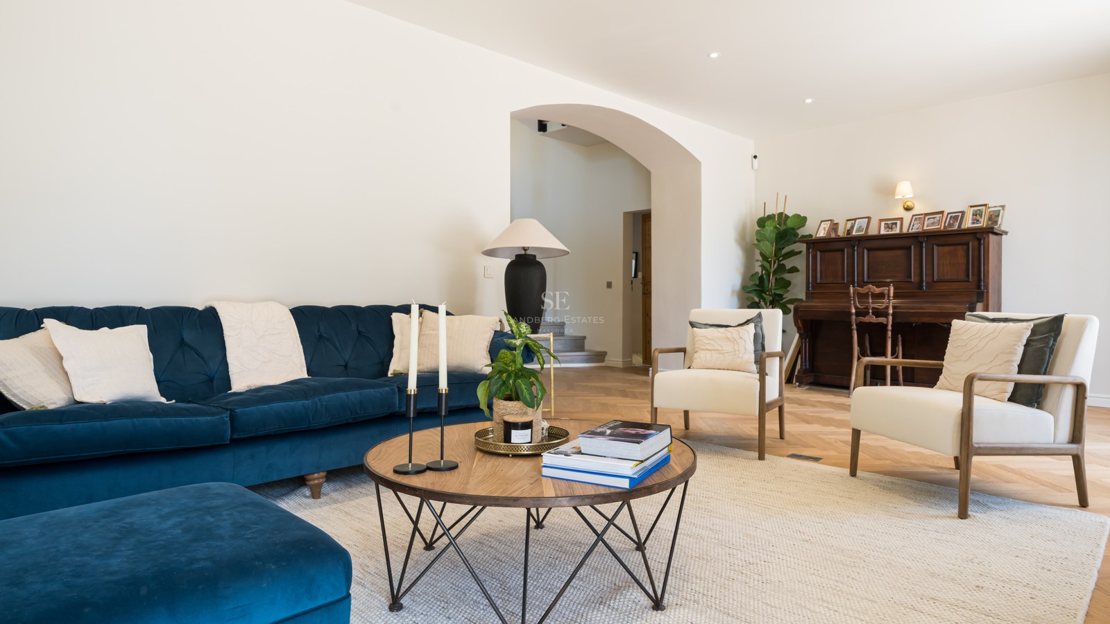Luxury living room featuring a navy blue velvet sofa, herringbone wood floors, and a classic piano in the background.