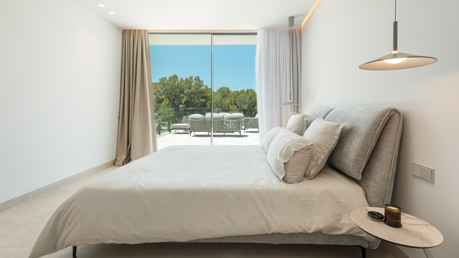 Chambre contemporaine avec grandes baies vitrées ouvrant sur une terrasse avec mobilier et vue sur les arbres.