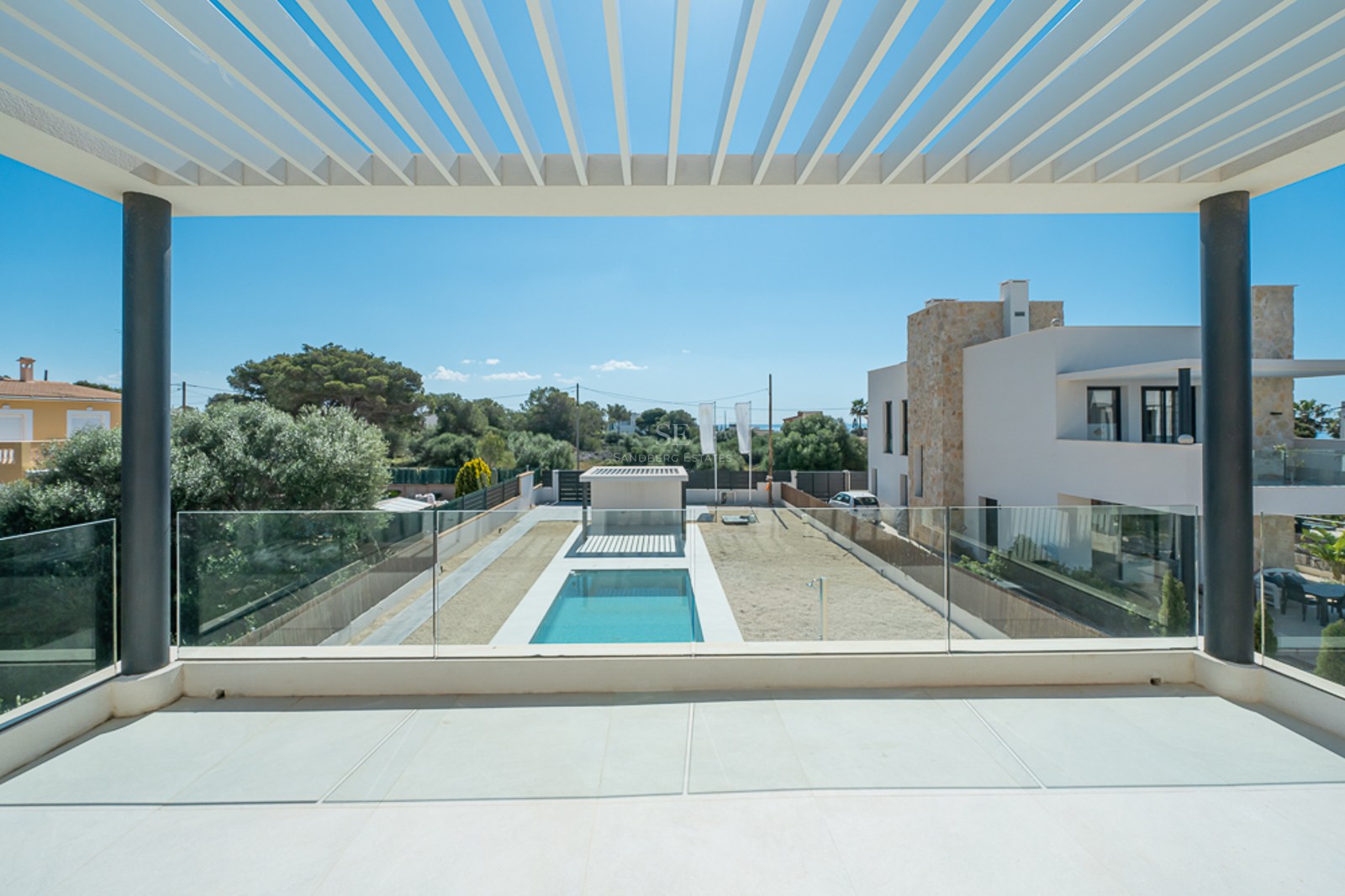 Vue depuis un balcon moderne avec pergola blanche et garde-corps en verre donnant sur une piscine et un jardin.
