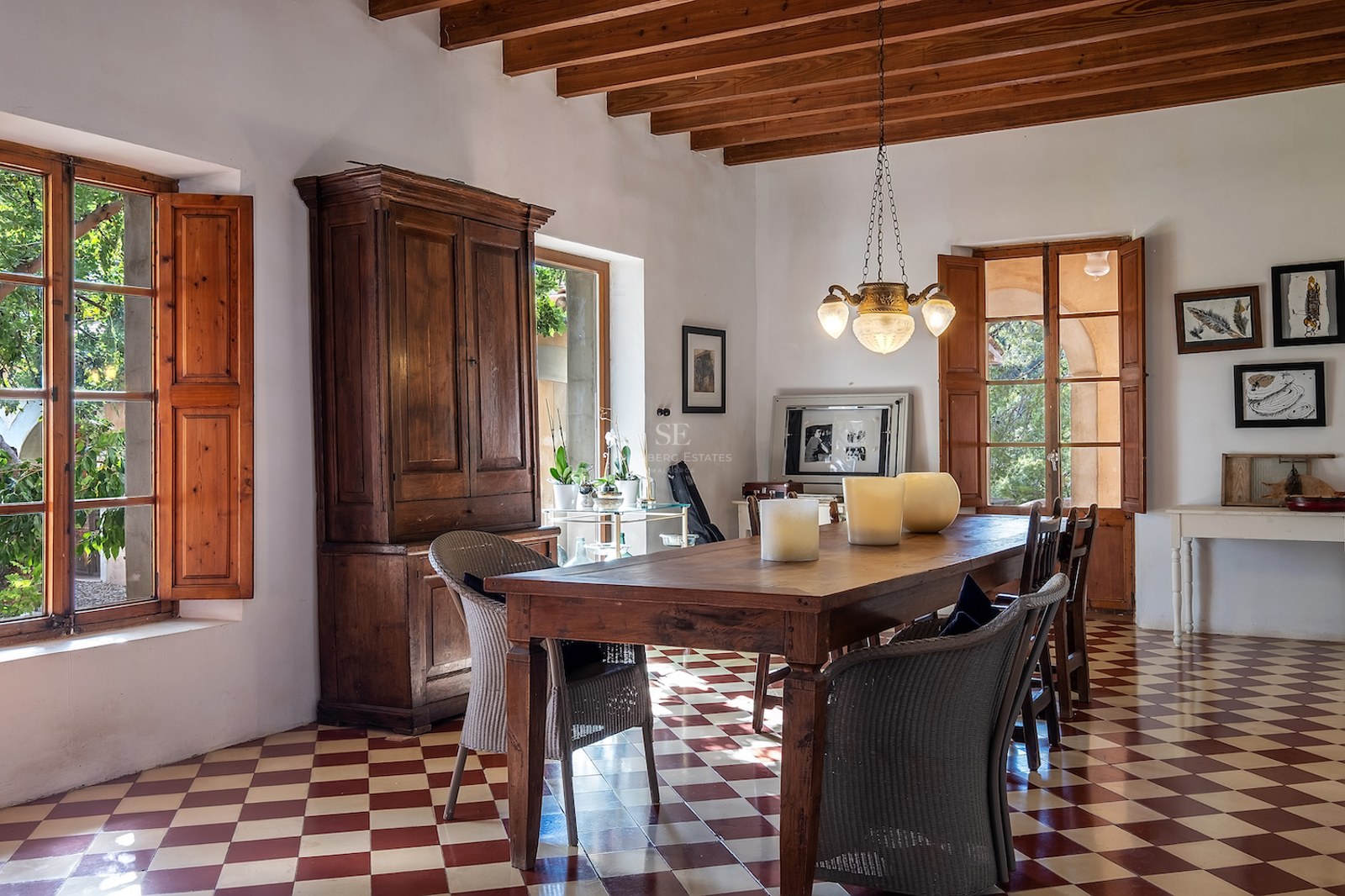 Salle à manger rustique avec table en bois, sol en damier rouge et blanc et poutres apparentes.
