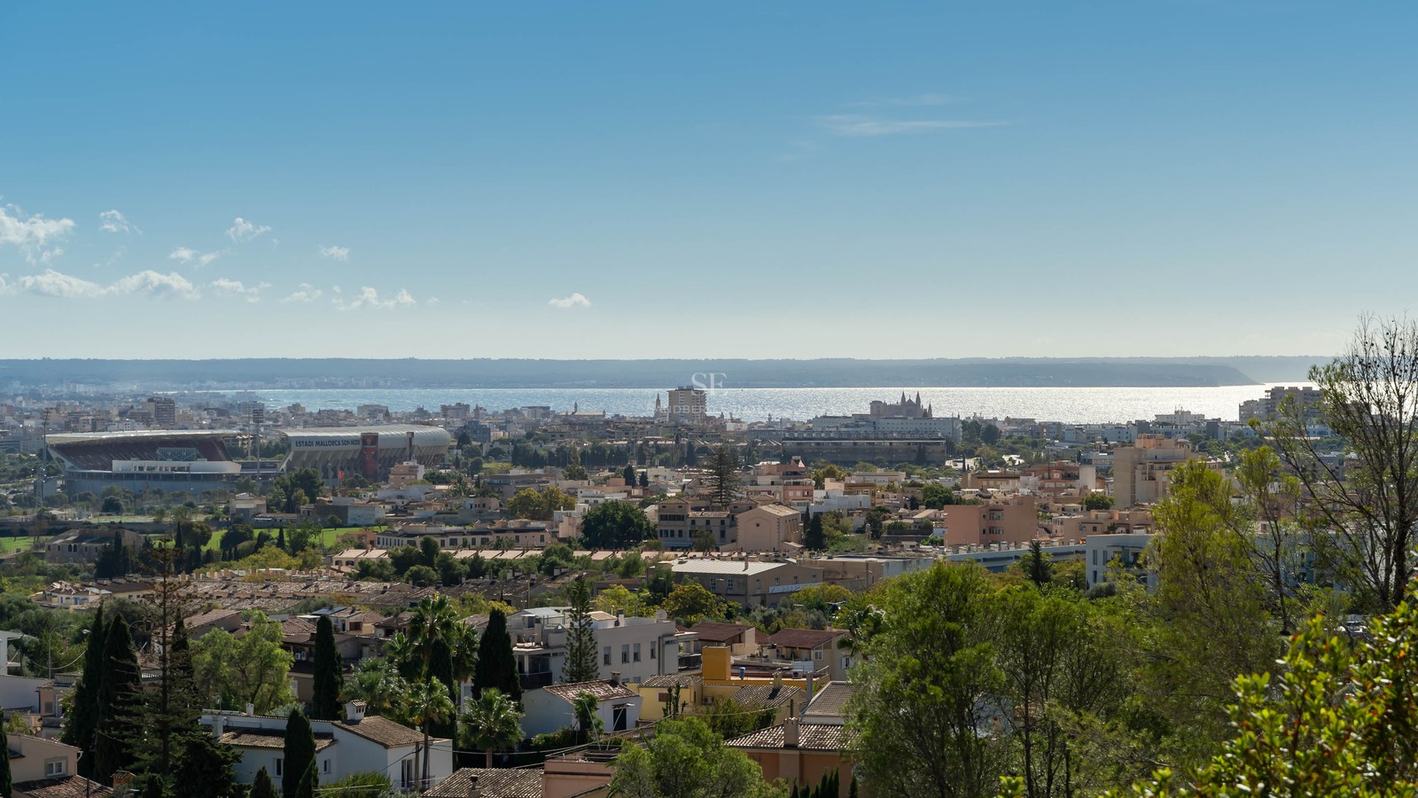 Vista panorámica de Palma con edificios, árboles y el mar Mediterráneo resplandeciente bajo un cielo azul despejado.