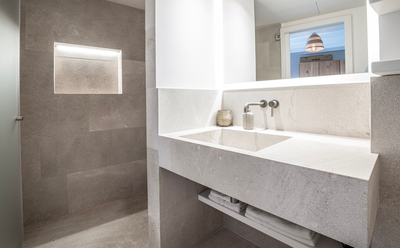 Modern stone bathroom featuring an integrated sink, wall-mounted faucet, and a glowing recessed niche in the stone wall.