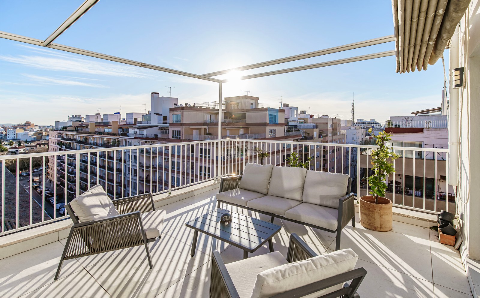Terrasse ensoleillée avec mobilier gris moderne, balustrades blanches et vue imprenable sur la ville.