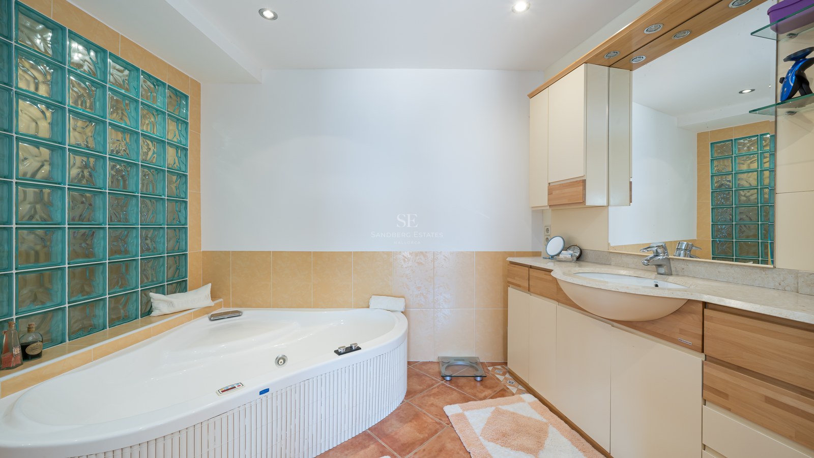 Interior view of a bathroom featuring a large corner whirlpool tub, turquoise glass blocks, and wood vanity.