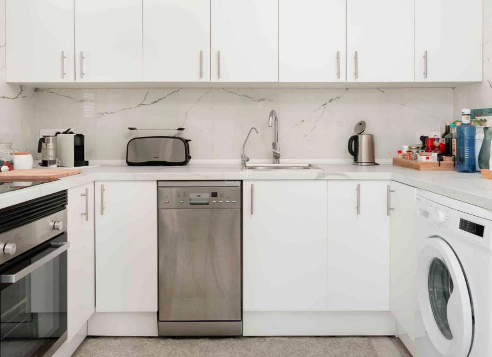 Modern white kitchen featuring marble countertops, stainless steel dishwasher, and minimalist cabinetry.