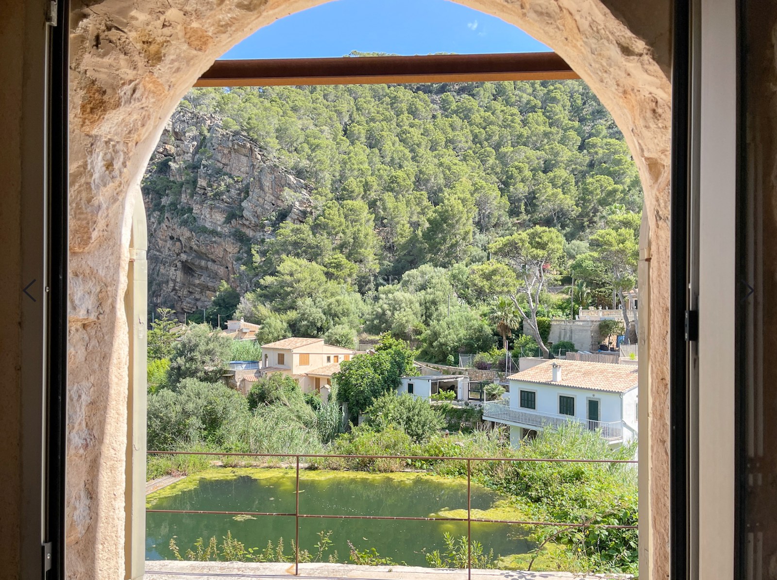 Vista a través de un arco de piedra natural de un valle verde, acantilados y casas tradicionales mallorquinas.