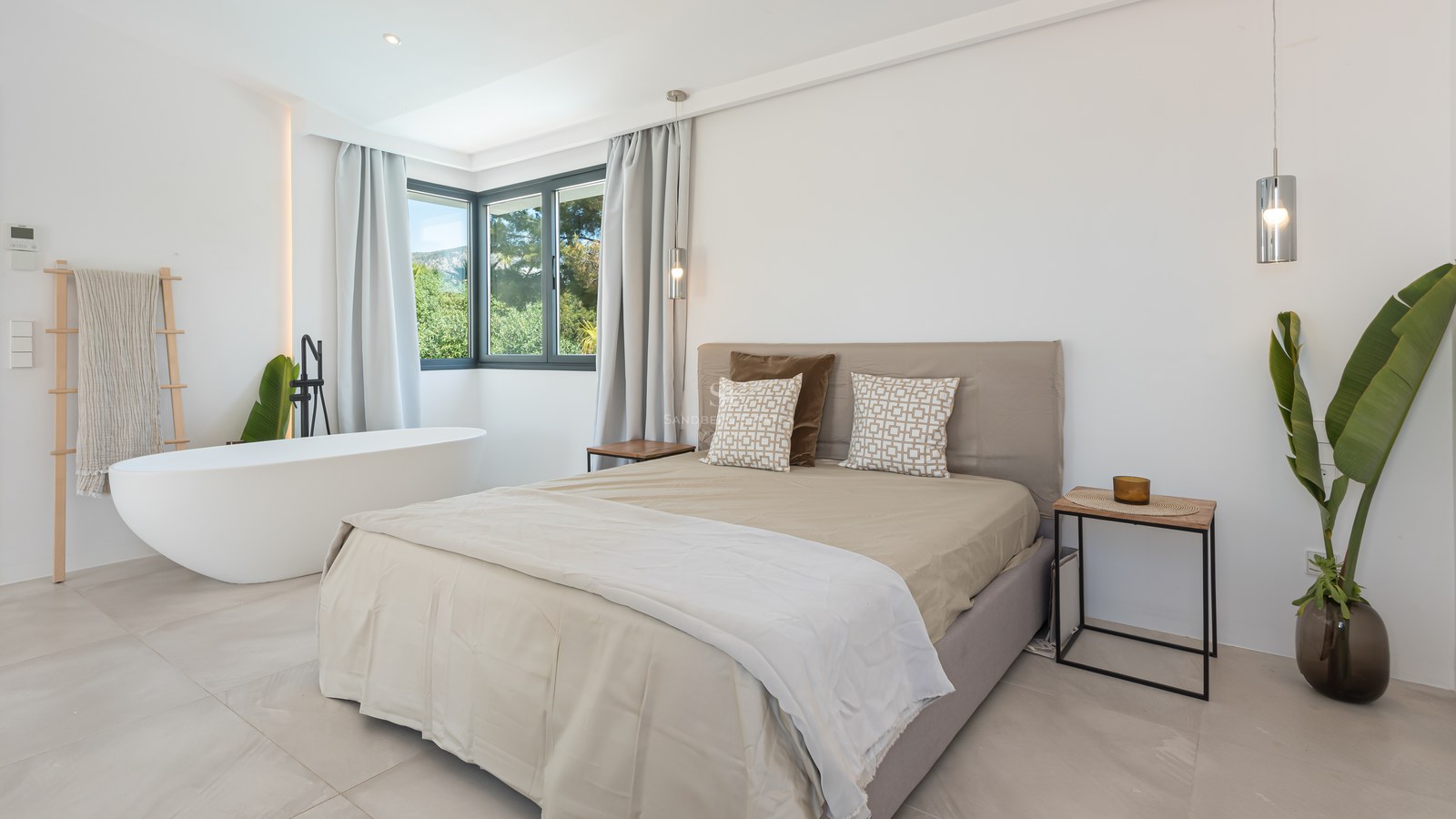 Minimalist bedroom featuring a white freestanding tub, neutral linens, and corner windows overlooking lush greenery.