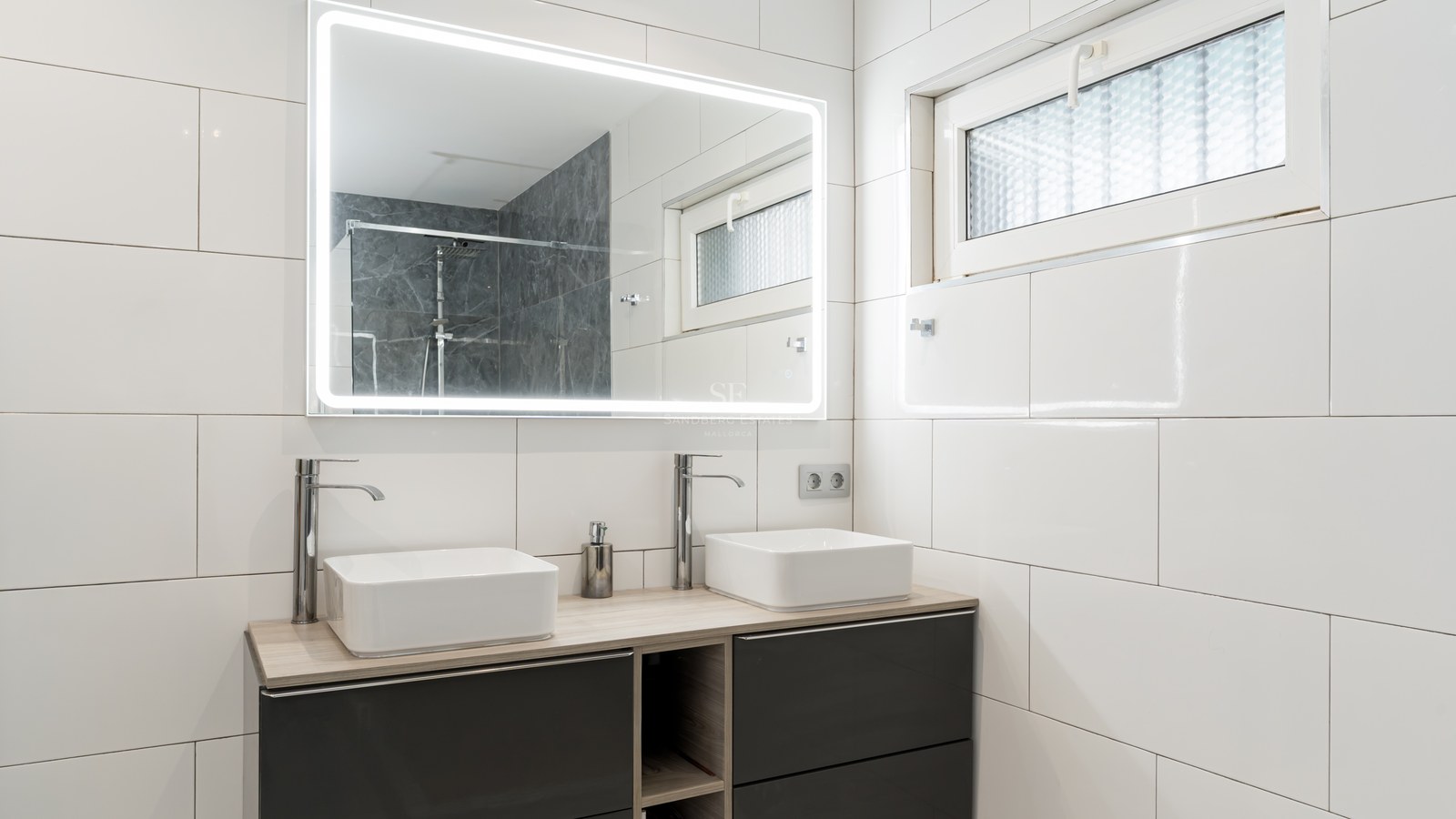 Modern bathroom featuring a double vanity with square sinks, a large LED backlit mirror, and white tiled walls.