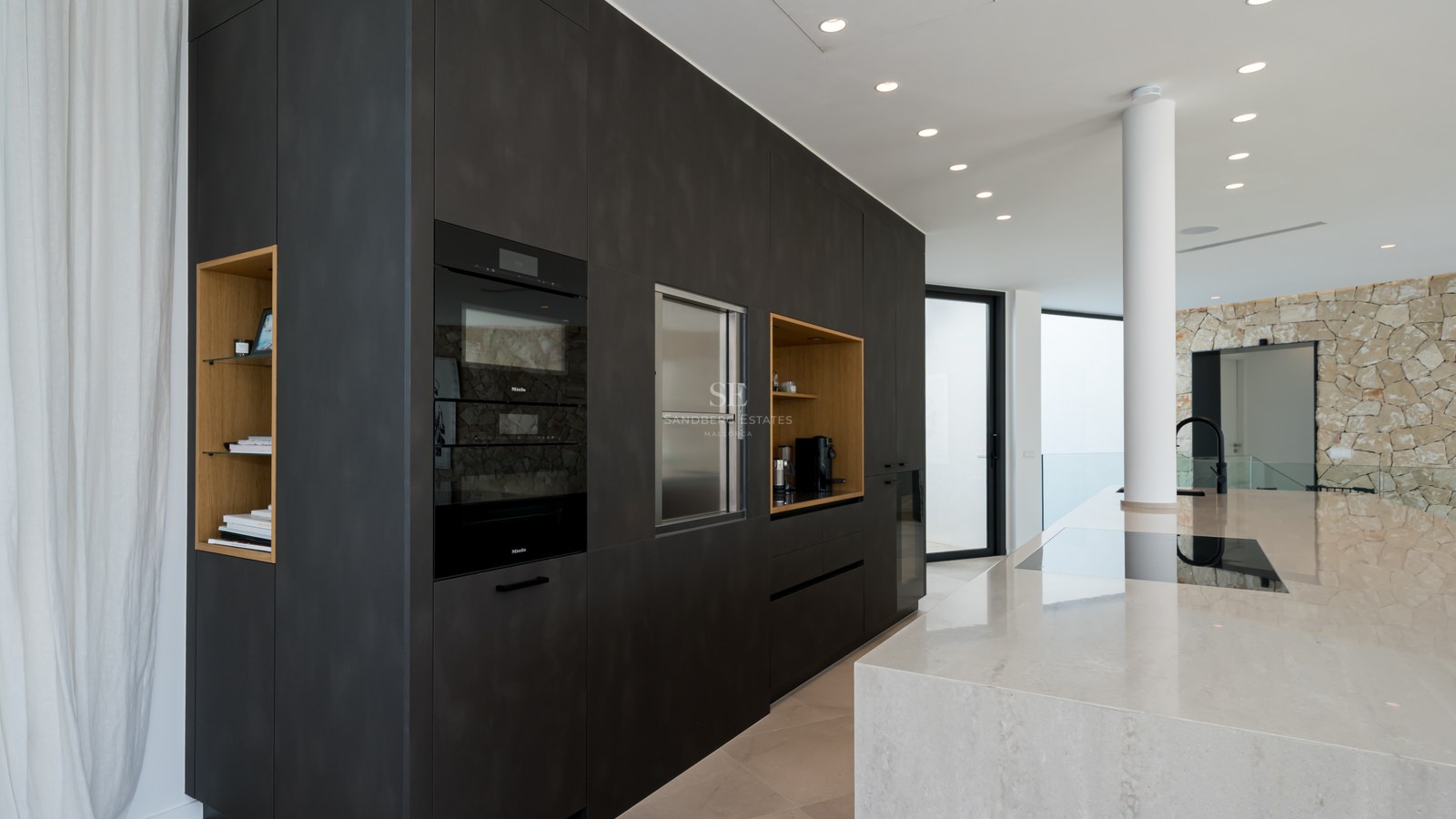 Cuisine moderne avec placards anthracite, îlot en marbre et fours Miele intégrés dans un espace lumineux.