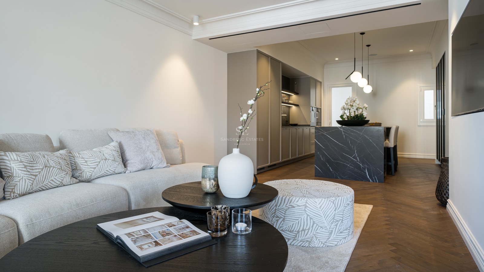 Salón contemporáneo y cocina integrados con suelos de espiga, isla de mármol oscuro y mobiliario en tonos neutros.